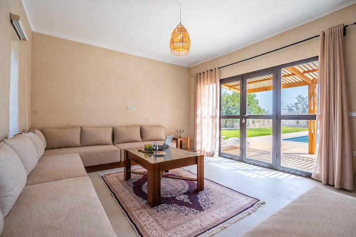 Salon avec canapé d’angle et baie vitrée donnant sur la piscine de la Villa Jnan Mogador.