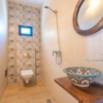 Salle de bains de la Villa Jnan Mogador avec douche, vasque décorée et miroir rond.